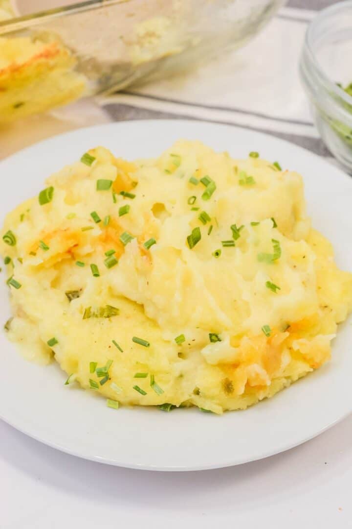 A serving of cheesy Baked Twice Mashed Potatoes topped with chopped chives is presented on a white plate for a comforting, savory dish.