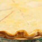 Close-up of a baked pie with a golden, crimped Crisco Pie Crust in a glass dish, partially visible next to a red and white striped cloth.