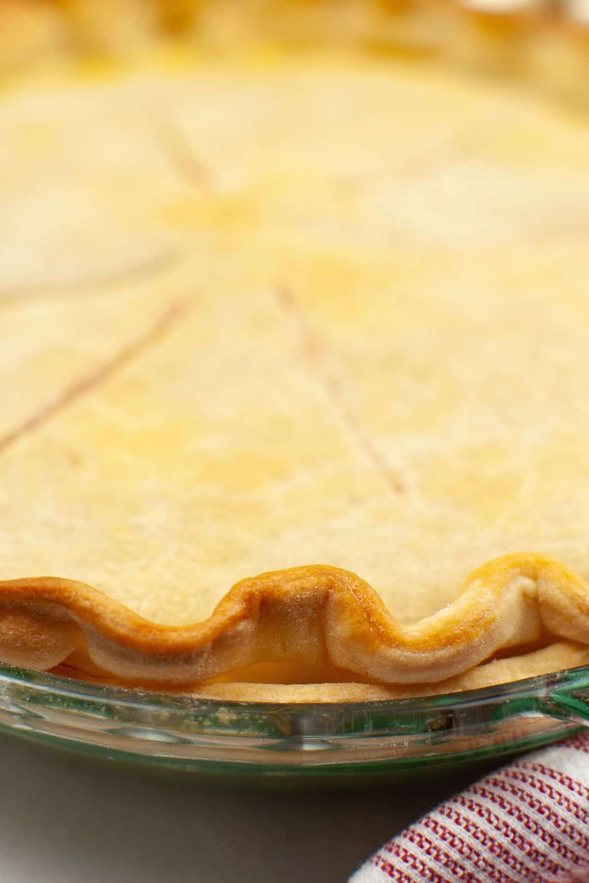 Close-up of a baked pie with a golden, crimped Crisco Pie Crust in a glass dish, partially visible next to a red and white striped cloth.