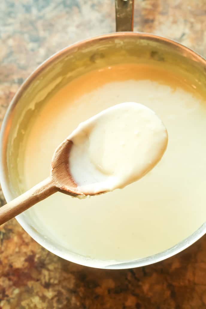 Traditional alfredo sauce on a spoon over a pot.