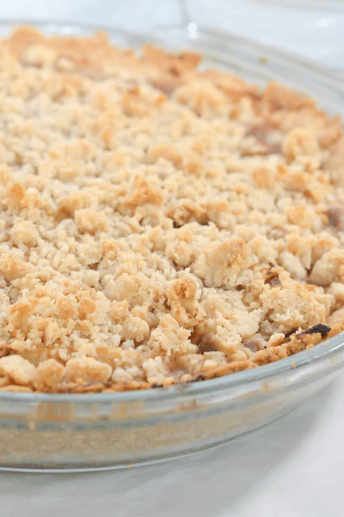 Close-up of a freshly baked, crumbly Easy Apple Pie with a golden-brown topping in a clear glass pie dish.