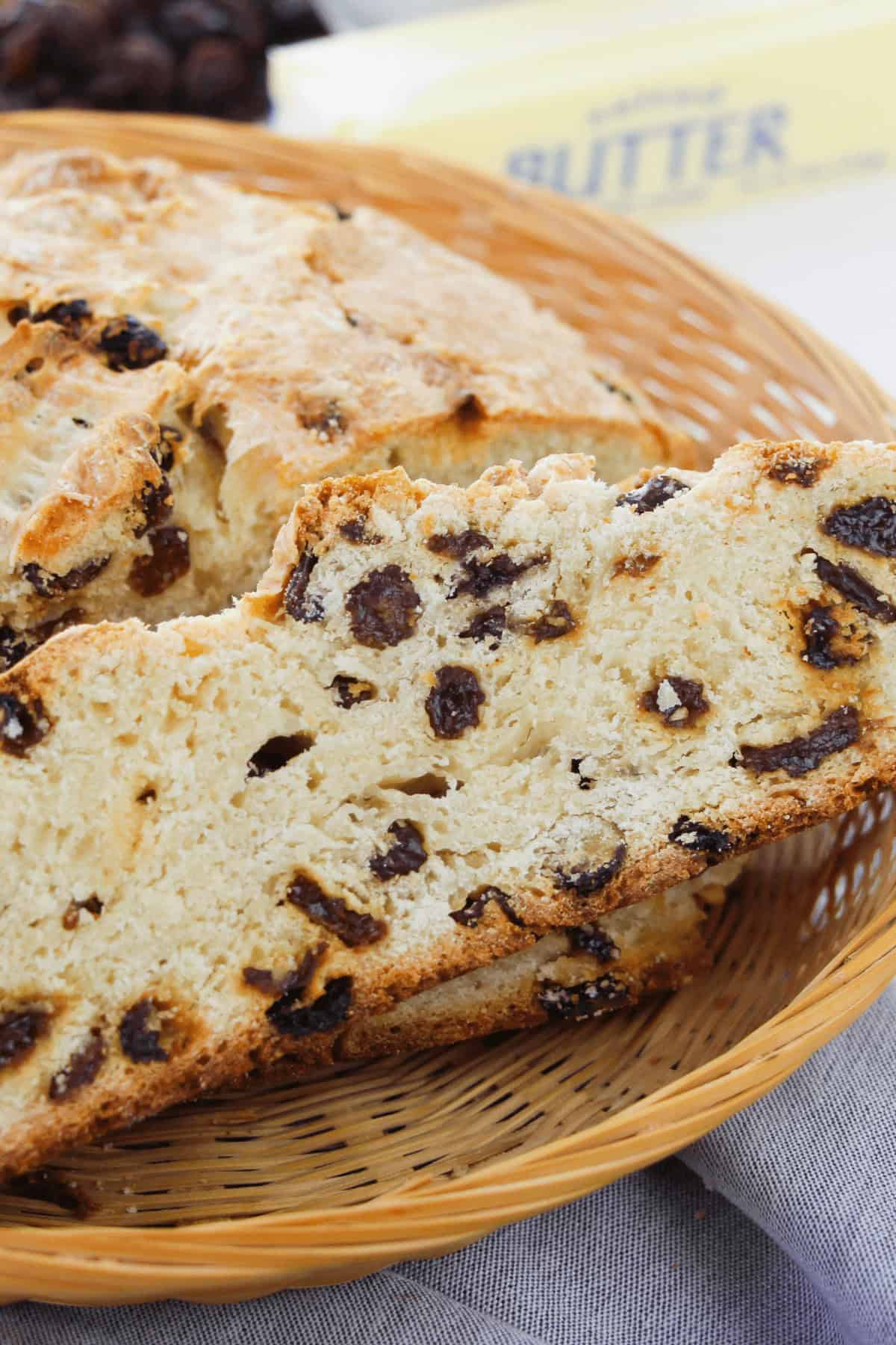 A slice  of easy Irish soda bread, rests in a wicker basket with a butter package visible in the background.