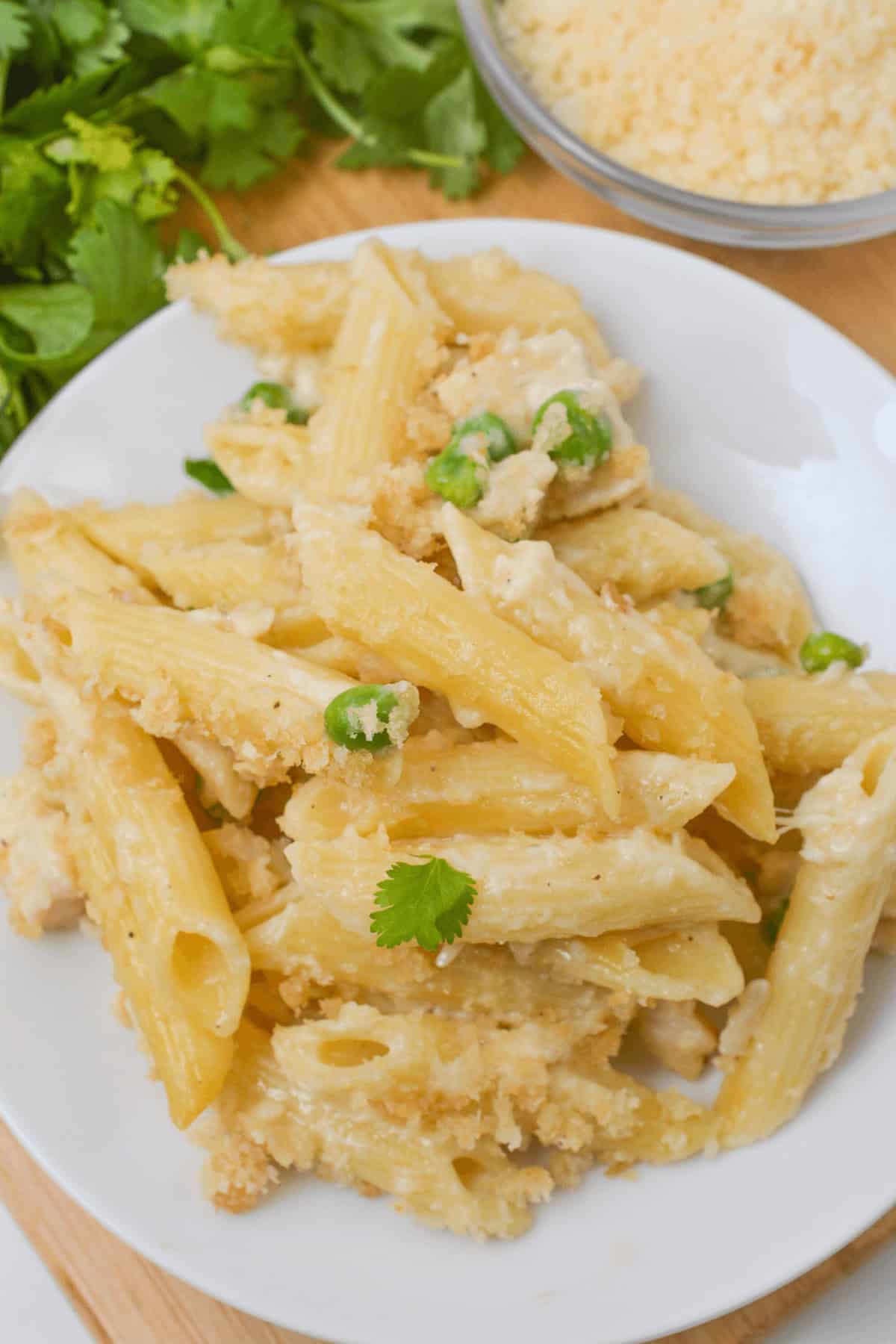 A plate of garlic Parmesan pasta with baked penne, tender chicken, and peas swimming in a creamy sauce, topped with a sprinkle of cheese and garnished with a fresh cilantro leaf.