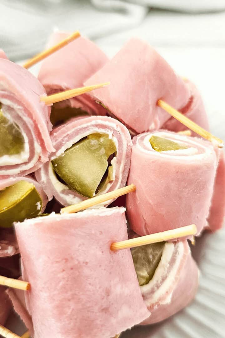 Pickle Roll Ups feature ham rolled with creamy cheese and tangy pickles, all neatly secured with toothpicks on a pristine white plate.