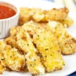 A plate of crispy Air Fryer Mozzarella sticks served with a small bowl of marinara sauce on the side, all arranged on a white plate.