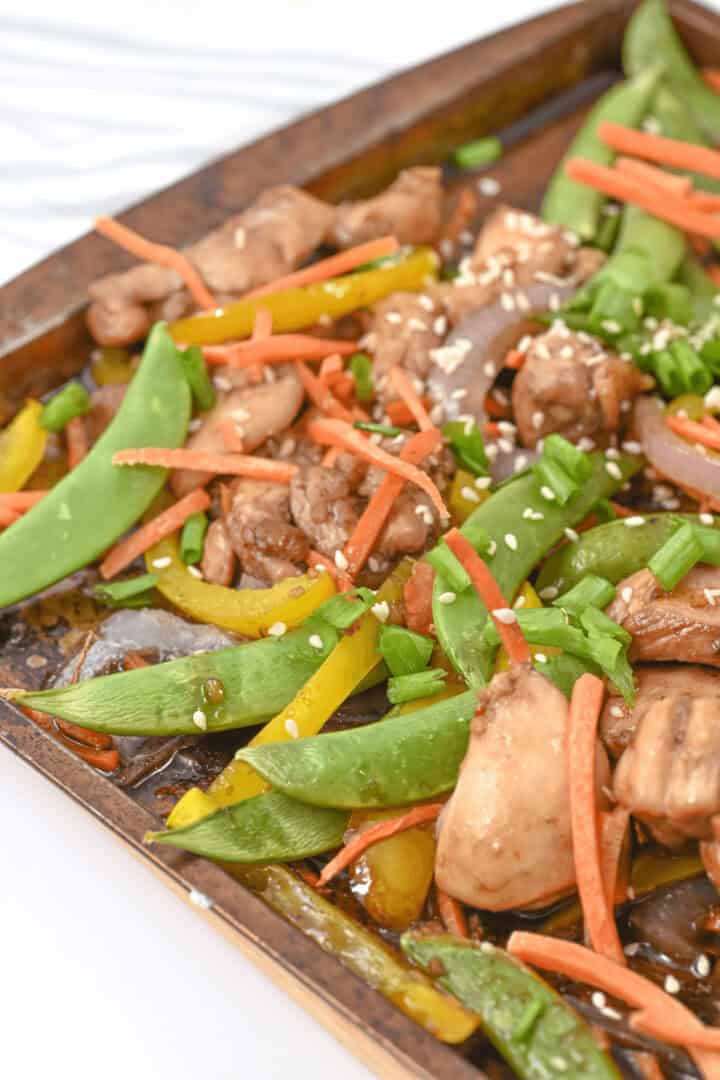 A tray of meal features stir-fried snow peas, bell peppers, and carrots, all topped with sesame seeds and chopped green onions.