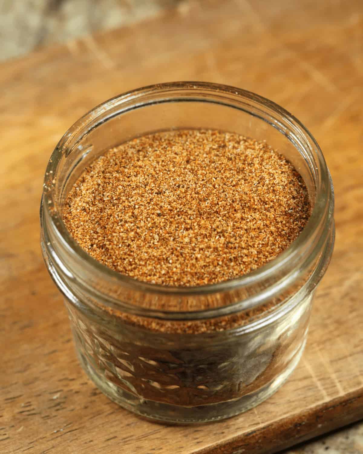 A glass jar filled with low sodium taco seasoning on a wooden surface.