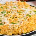 A plate of creamy pumpkin risotto topped with grated cheese and chopped herbs, placed on a white checkered cloth.