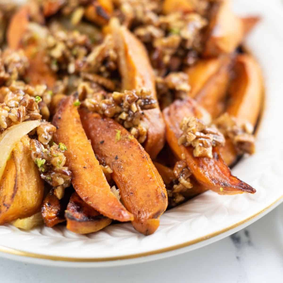 Plate of Roasted Spicy Sweet Potatoes wedges topped with chopped walnuts and herbs.