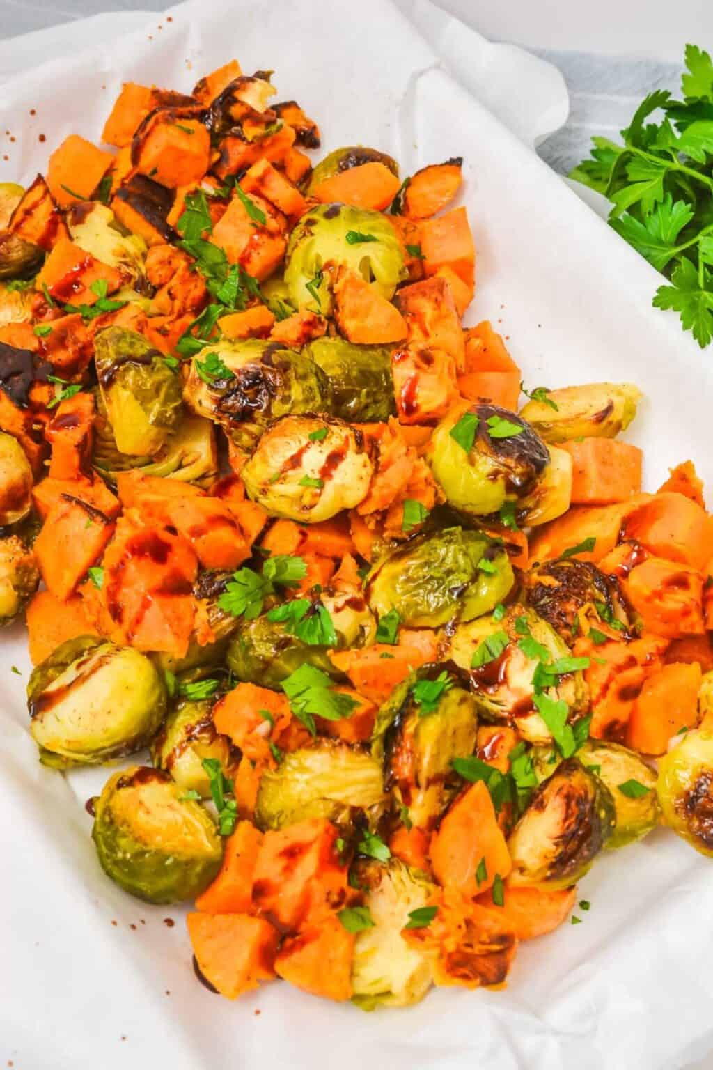Roasted Brussels sprouts and sweet potatoes, classic roasted vegetables, are garnished with chopped parsley and served on a parchment-lined tray.